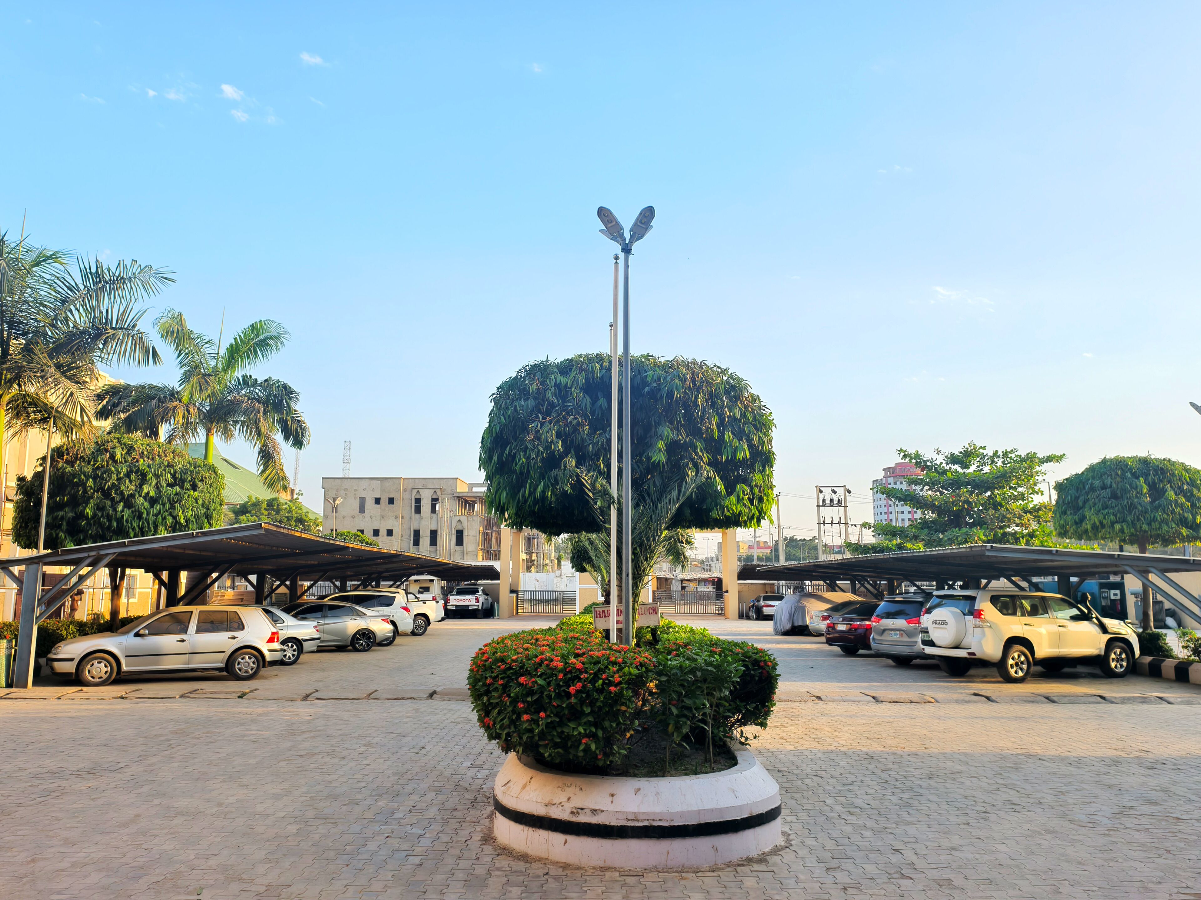 A parking area with multiple cars, a central roundabout with a decorative bush, and a tall street lamp.