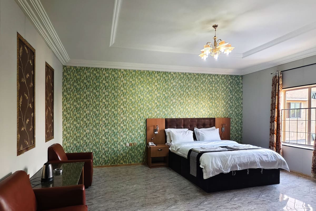 A hotel room with a large bed, a wooden headboard, a desk with a chair, a small table, and a green patterned wall.