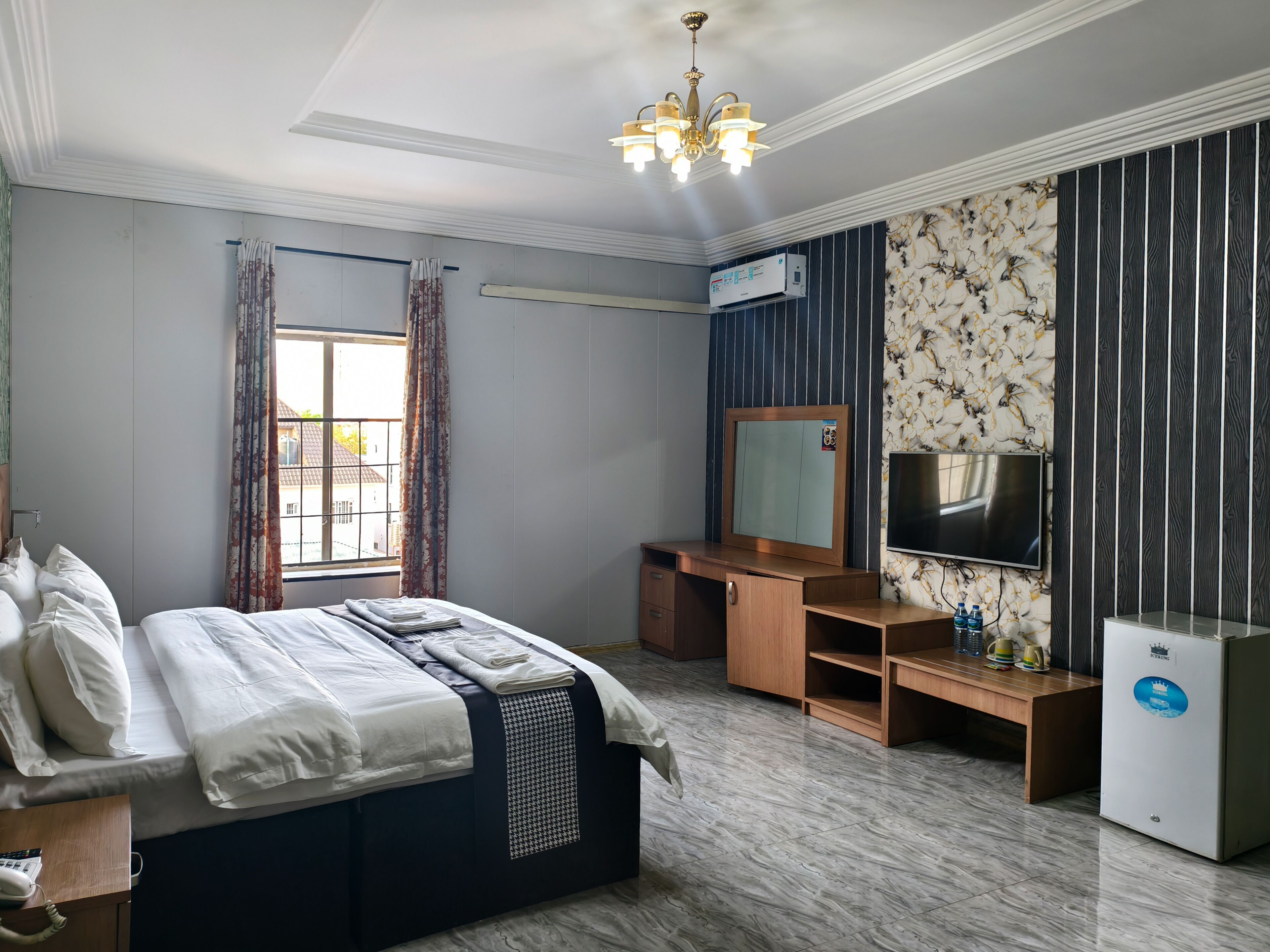 A bedroom with a bed, a vanity with a mirror, a television, and a refrigerator.