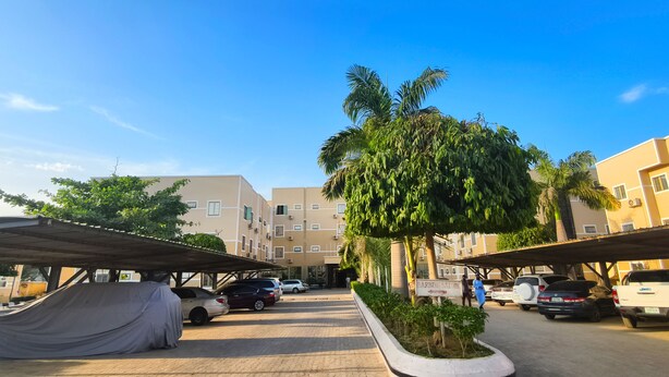 A parking area with covered carports, a sign for 'Farming Salons', and a row of parked cars. - Jun Yue No. 9 Hotel  (Kano)