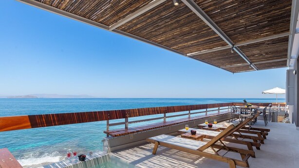 Un espace aménagé au bord de la piscine, avec vue sur la mer, comprenant des chaises longues en bois et une table avec des boissons.