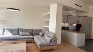 Un salon moderne avec un canapé d’angle gris, une table basse en bois et un luminaire suspendu.
