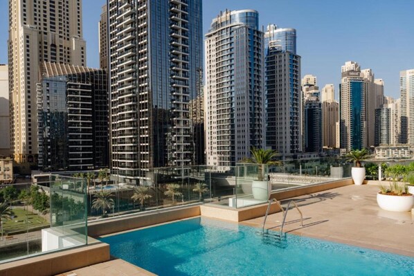 Piscina no terraço com guarda-corpo de vidro, cercada por edifícios altos.