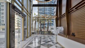 Un moderno vestíbulo de hotel con piso de diseño geométrico, amplias puertas de vidrio y vista a un rascacielos.