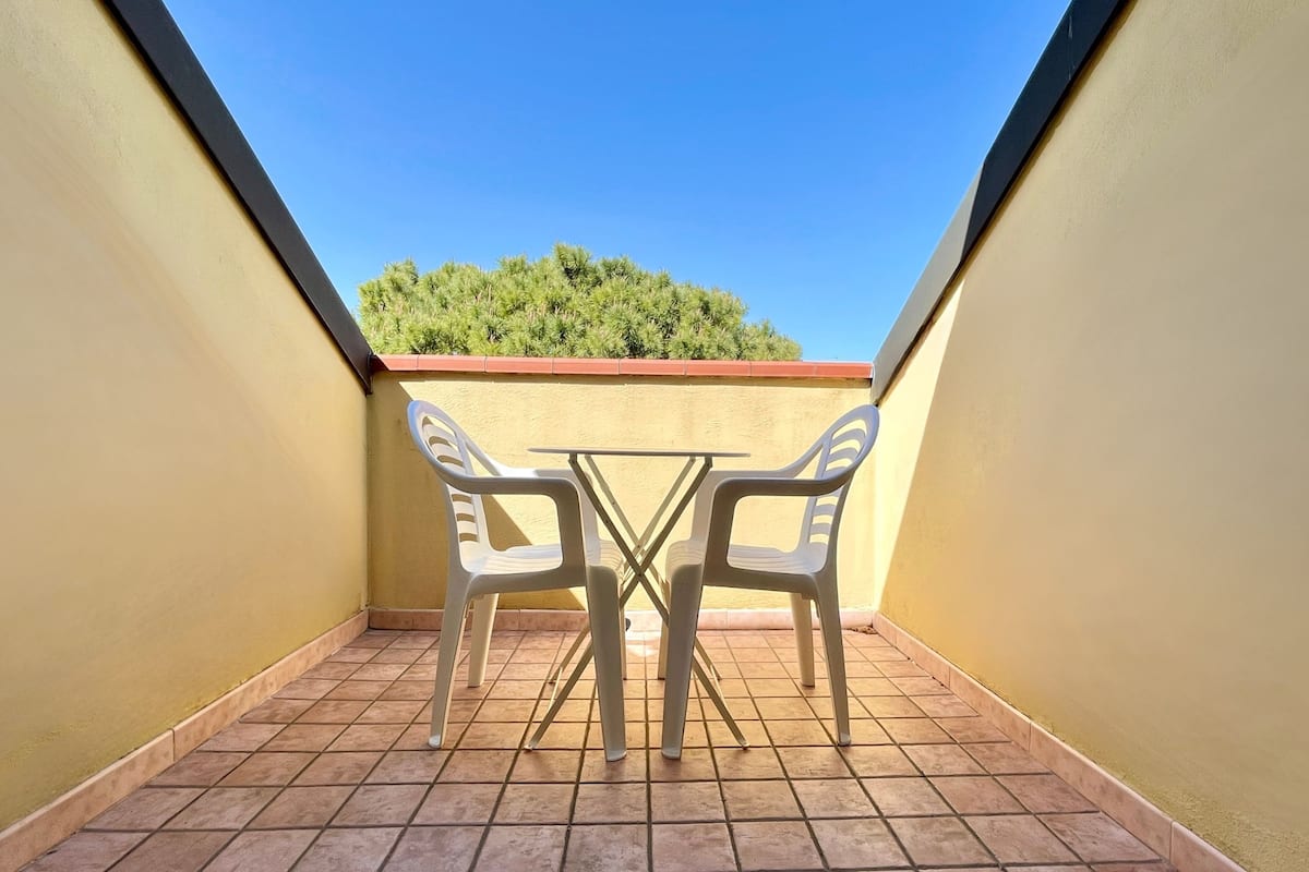A small balcony with a tiled floor, two white plastic chairs, and a small table.