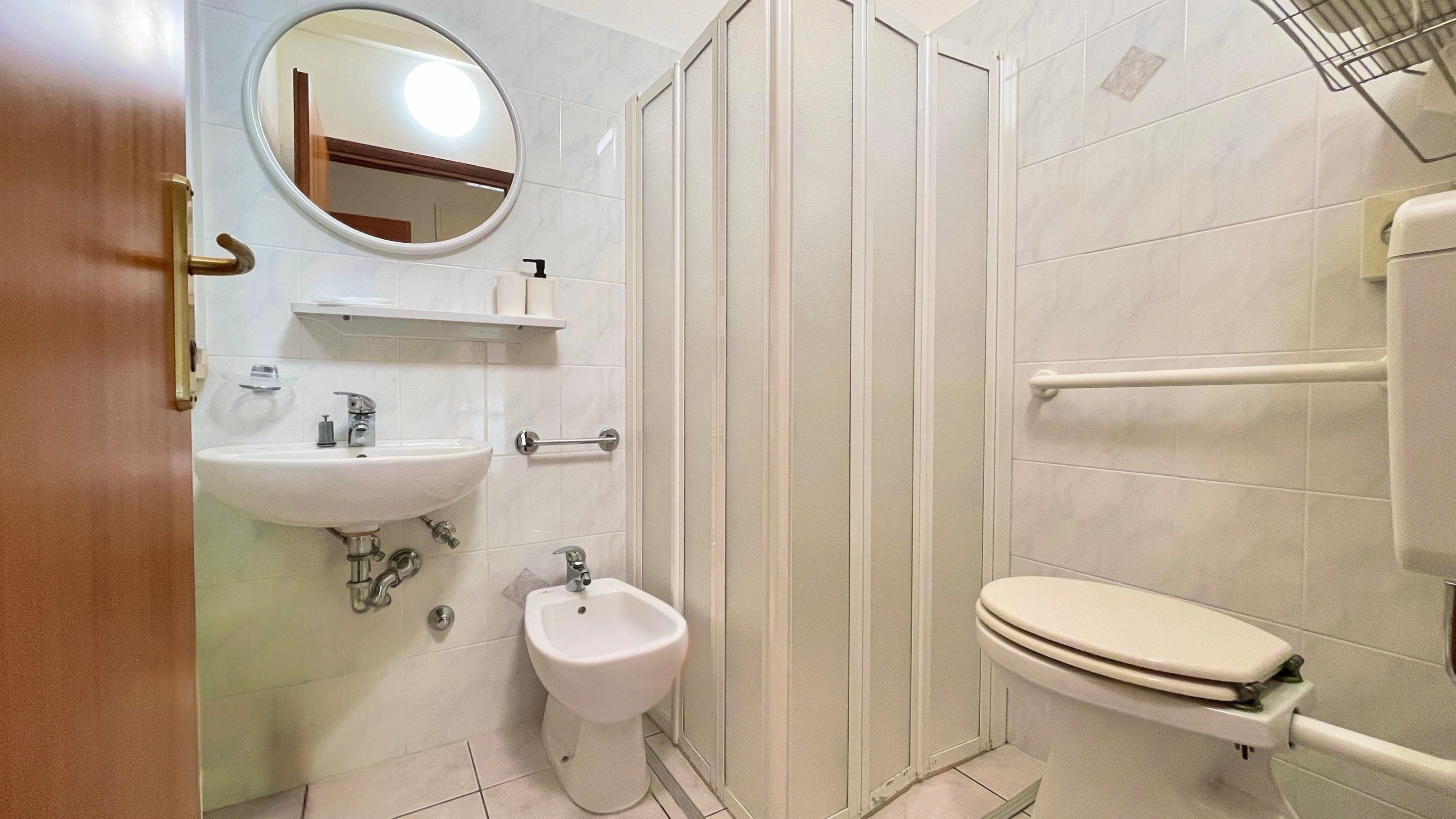 A bathroom with a sink, bidet, toilet, and a shower enclosure.