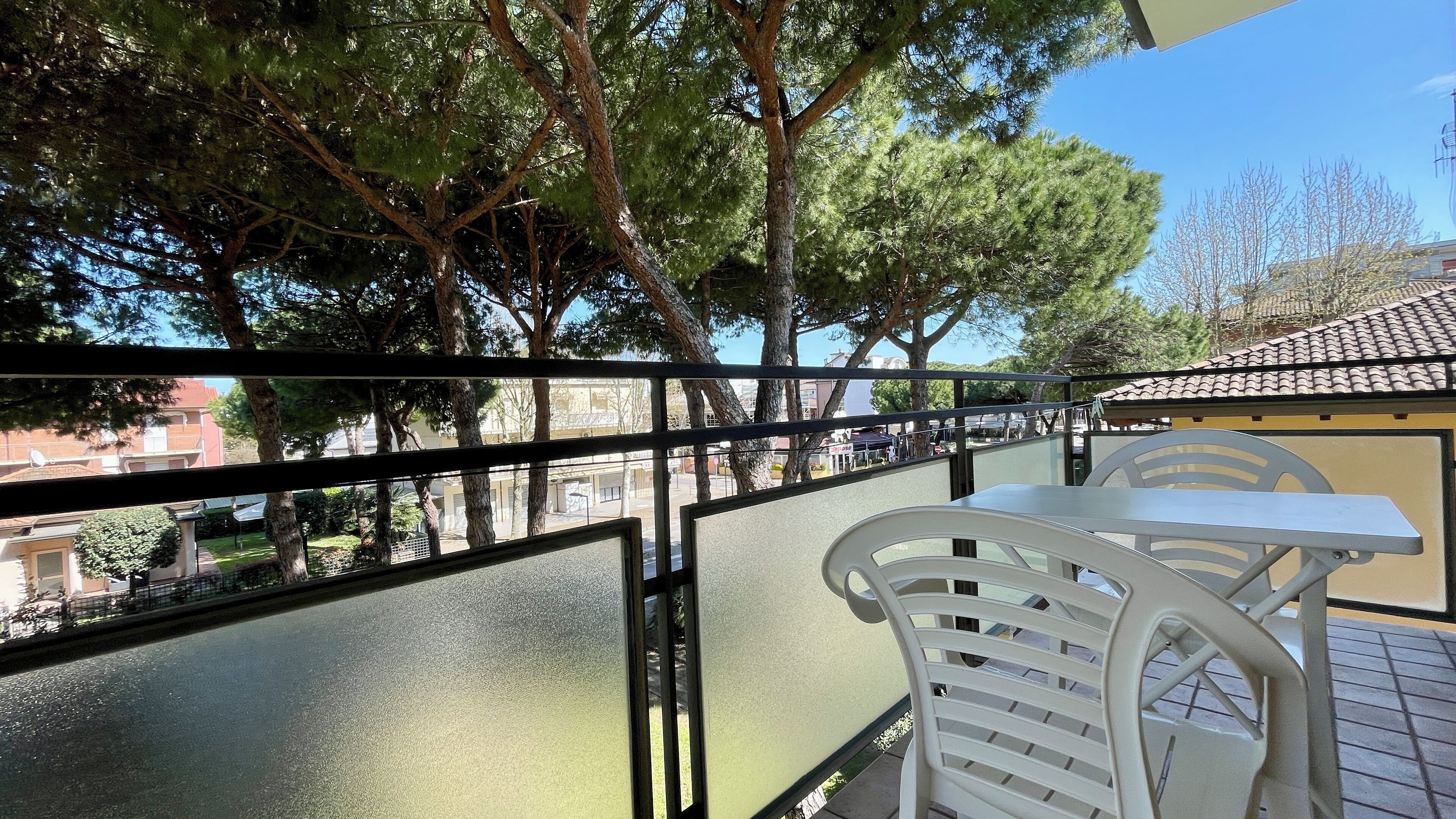 A balcony with a table and chairs, overlooking a street with trees and buildings.
