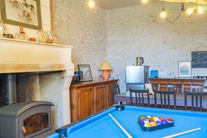 Una mesa de billar con bolas, una chimenea, un televisor y una zona de bar con sillas.
