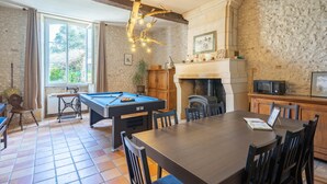 Una habitación con mesa de billar, mesa de comedor y sillas, chimenea y pared de piedra.