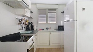 A compact kitchen with white cabinets, a black countertop, and a window with blinds. - The garden of Gavrelle (Gavrelle)