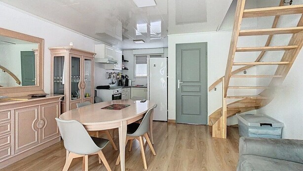 A compact kitchen with modern appliances, a dining area with a wooden table and chairs, and a wooden staircase leading to an upper level. - The garden of Gavrelle (Gavrelle)