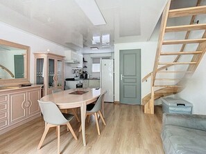 Una cucina compatta con elettrodomestici moderni, un'area pranzo con tavolo e sedie in legno, e una scala in legno che conduce a un piano superiore.