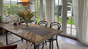 Zona pranzo con tavolo in legno, sedie, un vaso con fiori e un lampadario.