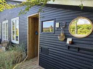 A wooden cabin with a door, windows, a mirror, and a small shelf with items. - "Yvette" - 350m from the sea by Interhome (Hejls)