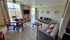 A living room with a dining table, chairs, a sofa, and a television. - Modern Ocean View 6 Sleeper King Suite with Wi-Fi, Underground Parking (Durban)