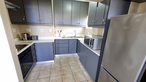 A compact kitchen with dark cabinets, a stainless steel refrigerator, a microwave, and a gas stove. - Modern Ocean View 6 Sleeper King Suite with Wi-Fi, Underground Parking (Durban)