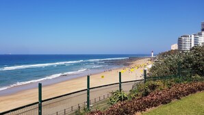 A beach with a fence, a lighthouse, and buildings in the background. - Modern Ocean View 6 Sleeper King Suite with Wi-Fi, Underground Parking (Durban)