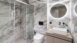 Un baño moderno con ducha de vidrio, inodoro blanco y tocador con un espejo grande.