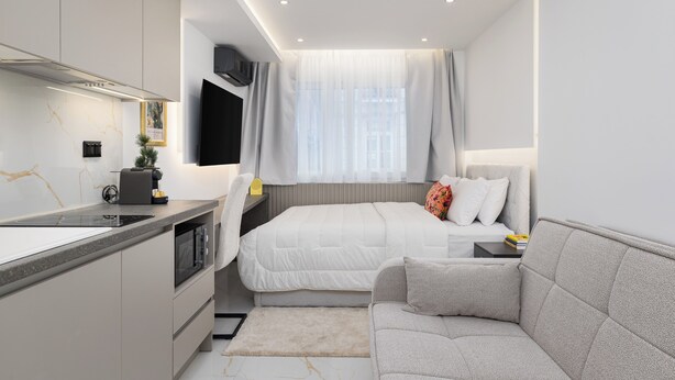 Un dormitorio moderno con cama, sofá, zona de cocina y ventana con cortinas.