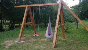A wooden swing set in a grassy area with trees in the background.