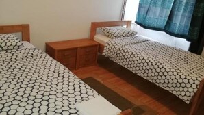 A small, tidy bedroom with two single beds, a wooden nightstand, and a window with curtains.