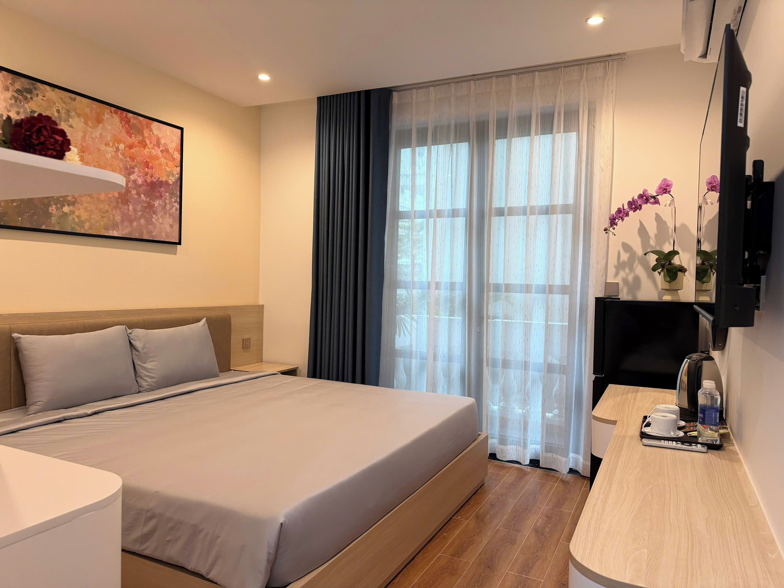 Ein Hotelzimmer mit einem großen Bett, einem Schreibtisch mit Stuhl, einem Fernseher und einem Fenster mit Vorhängen.