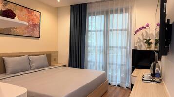 Ein Hotelzimmer mit einem großen Bett, einem Schreibtisch mit Stuhl, einem Fernseher und einem Fenster mit Vorhängen.