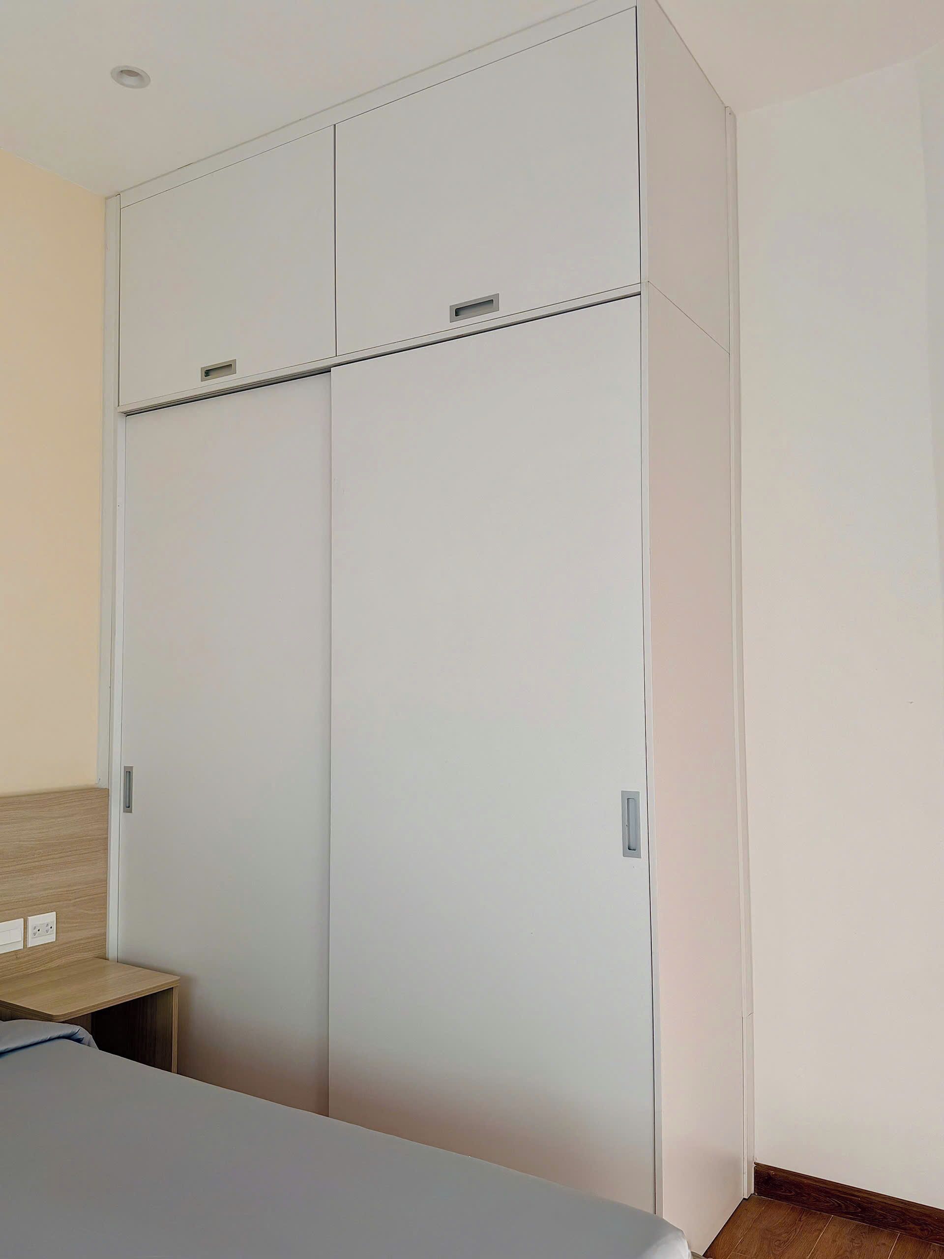 A bedroom with a large wardrobe, a bedside table, and a bed.