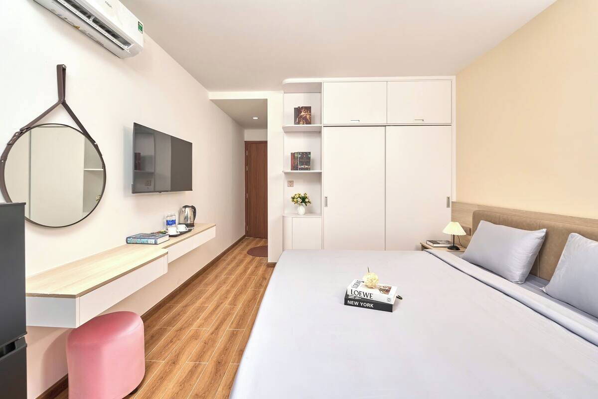 Habitación de hotel con cama, escritorio, silla, televisor, armario y espejo.
