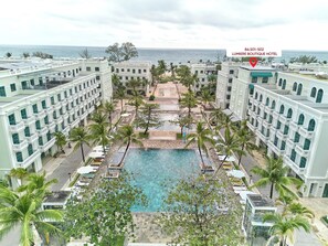 Un hotel con piscina rodeado de palmeras y vistas al océano.