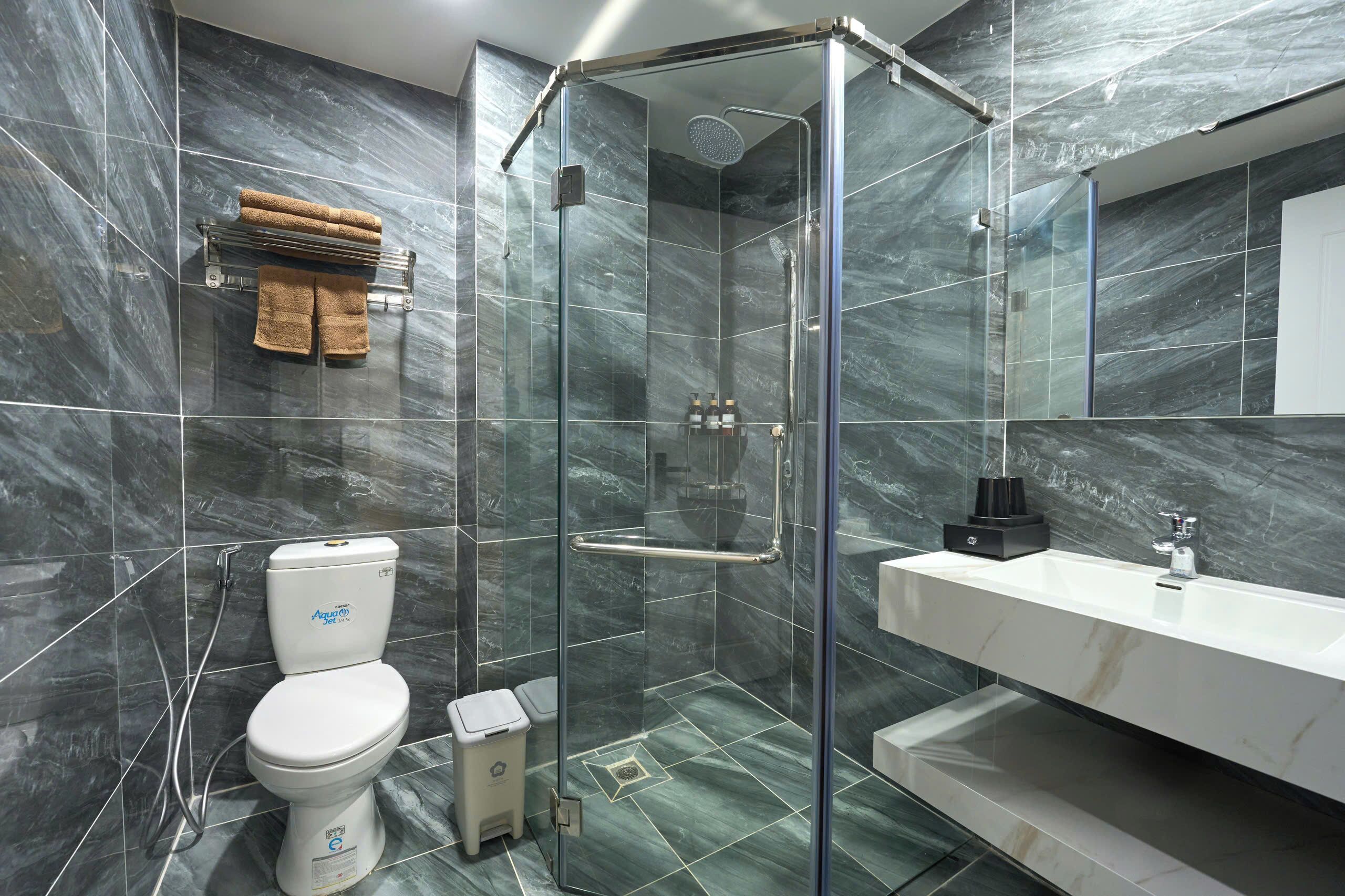 A modern bathroom with a glass-enclosed shower, a white toilet, a vanity with a mirror, and towels on a rack.