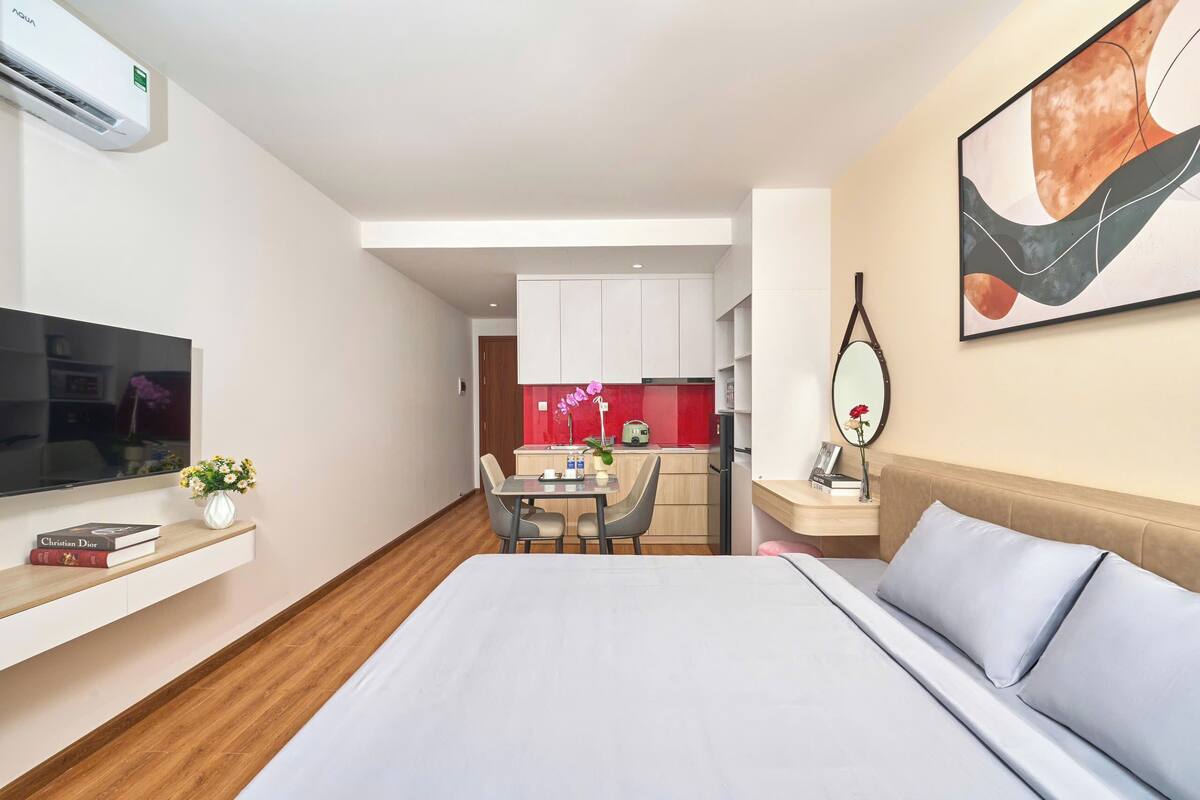Una habitación de hotel moderna con una cama, un televisor, un escritorio con una silla, una pequeña zona de cocina y un cuadro en la pared.