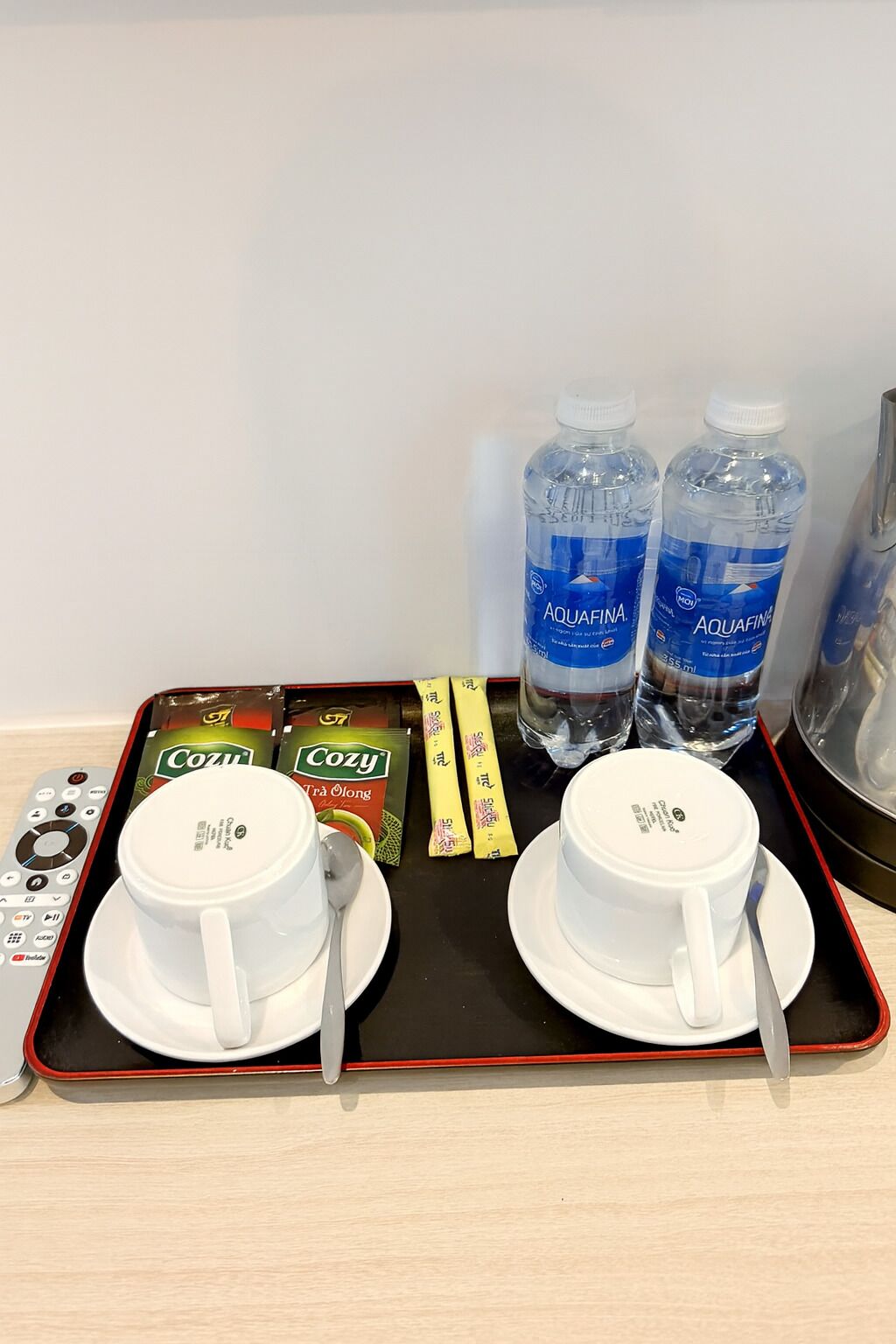 A tray with two white cups, two bottles of Aquafina water, and packets of Coozy tea.