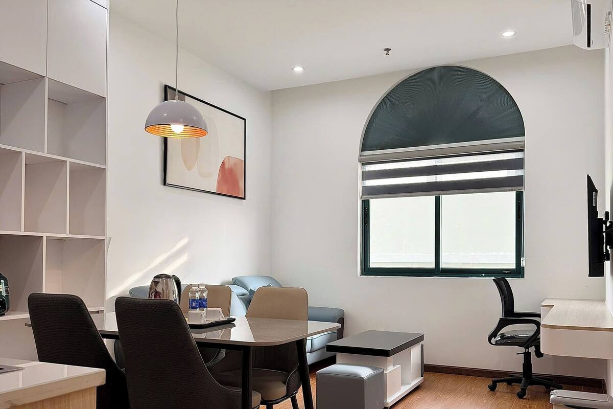 Una habitación moderna y luminosa con zona de comedor, sofá, ventana grande y estanterías empotradas.