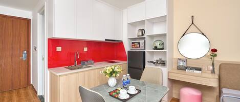 A compact kitchen with a red backsplash, a dining area with a table and chairs, a small pink stool, and a wall-mounted mirror.