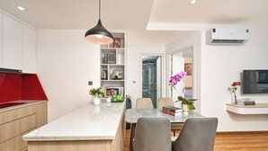 A modern kitchen with a central island, a dining area with two chairs, a red accent wall, and a TV on the wall. - Lumiere Boutique Phu Quoc Hotel (Phu Quoc)