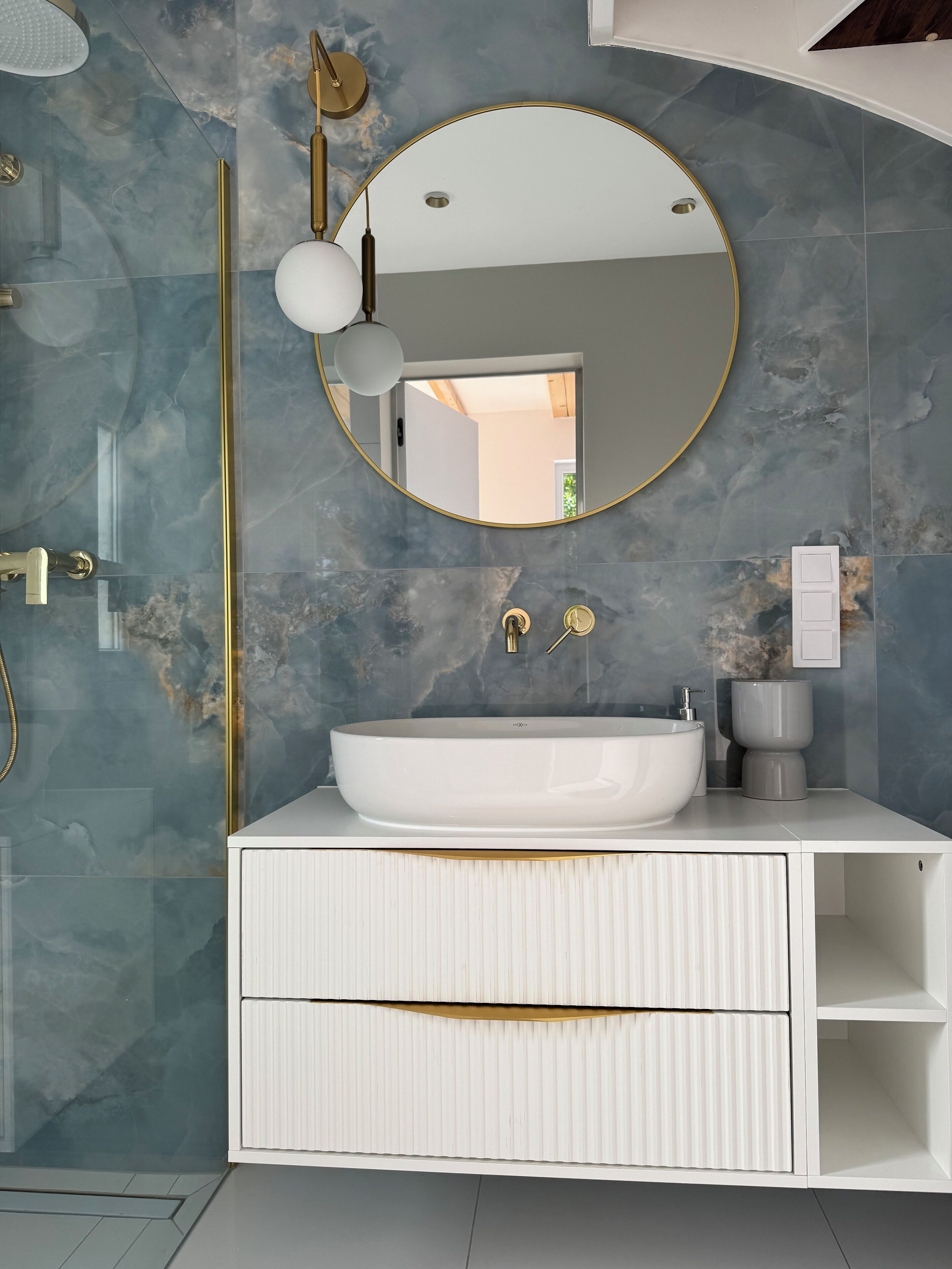 Un baño con tocador blanco, un espejo redondo y un lavabo grande.