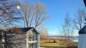 Egy modern ház terasszal, egy kis tárolóépülettel és fákkal beültetett, füves udvarral.