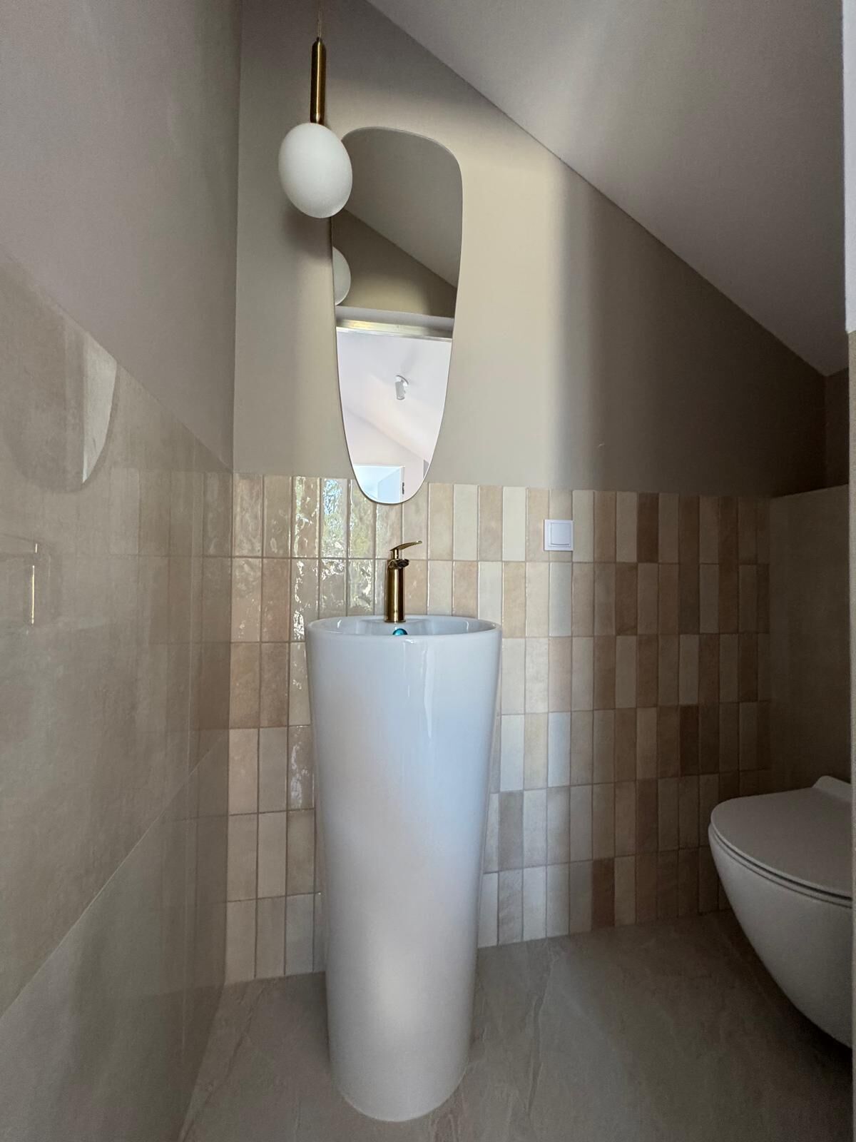 A bathroom with a large, white pedestal sink, a wall-mounted mirror, and a modern light fixture.