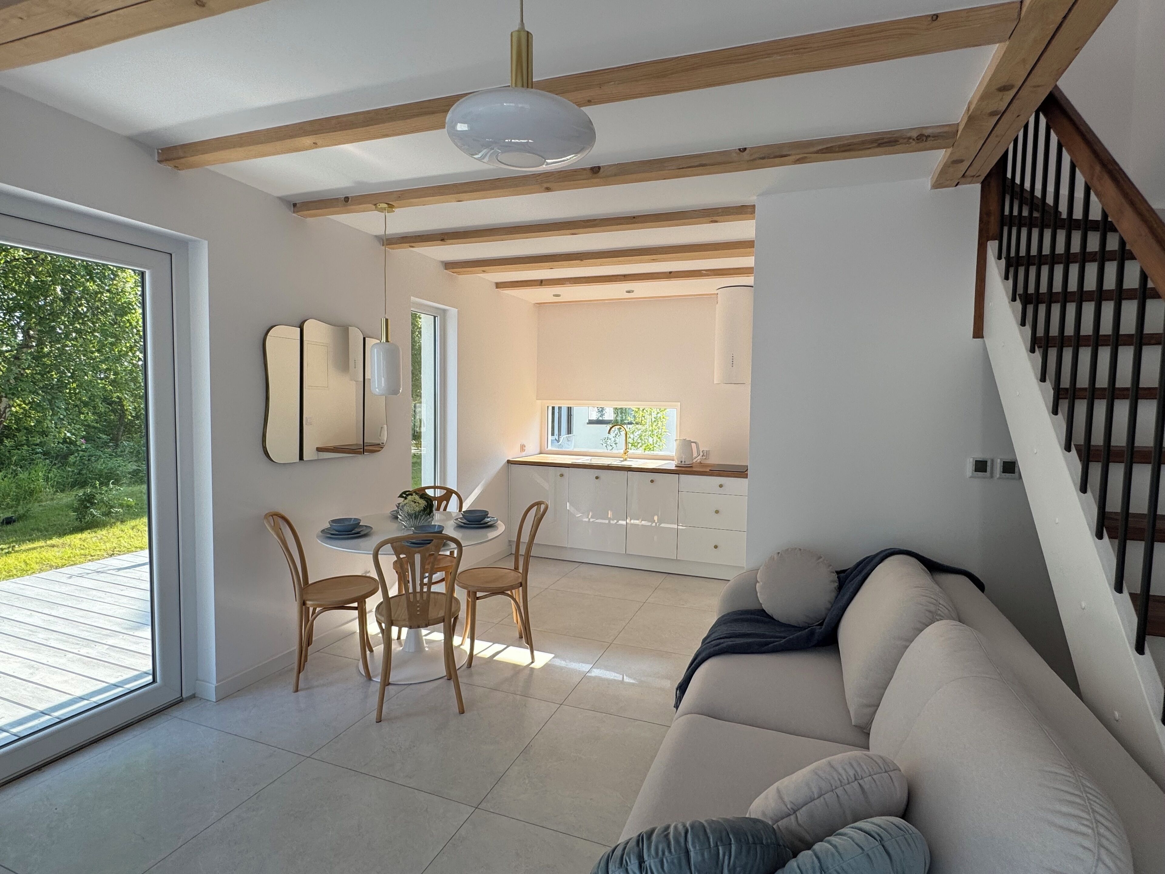 A modern living room with a sofa, dining table, and chairs. There is a kitchen area visible through an open door.
