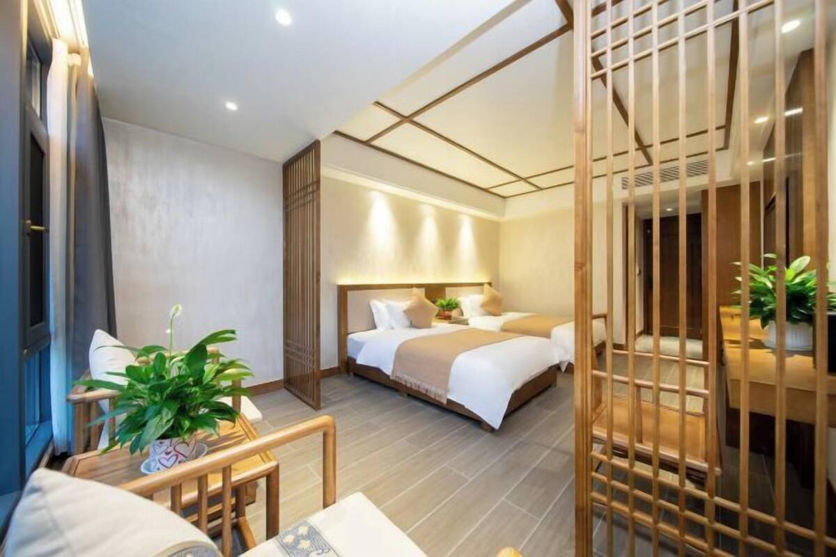 A hotel room with a bed, bedside table, chair, and a potted plant.