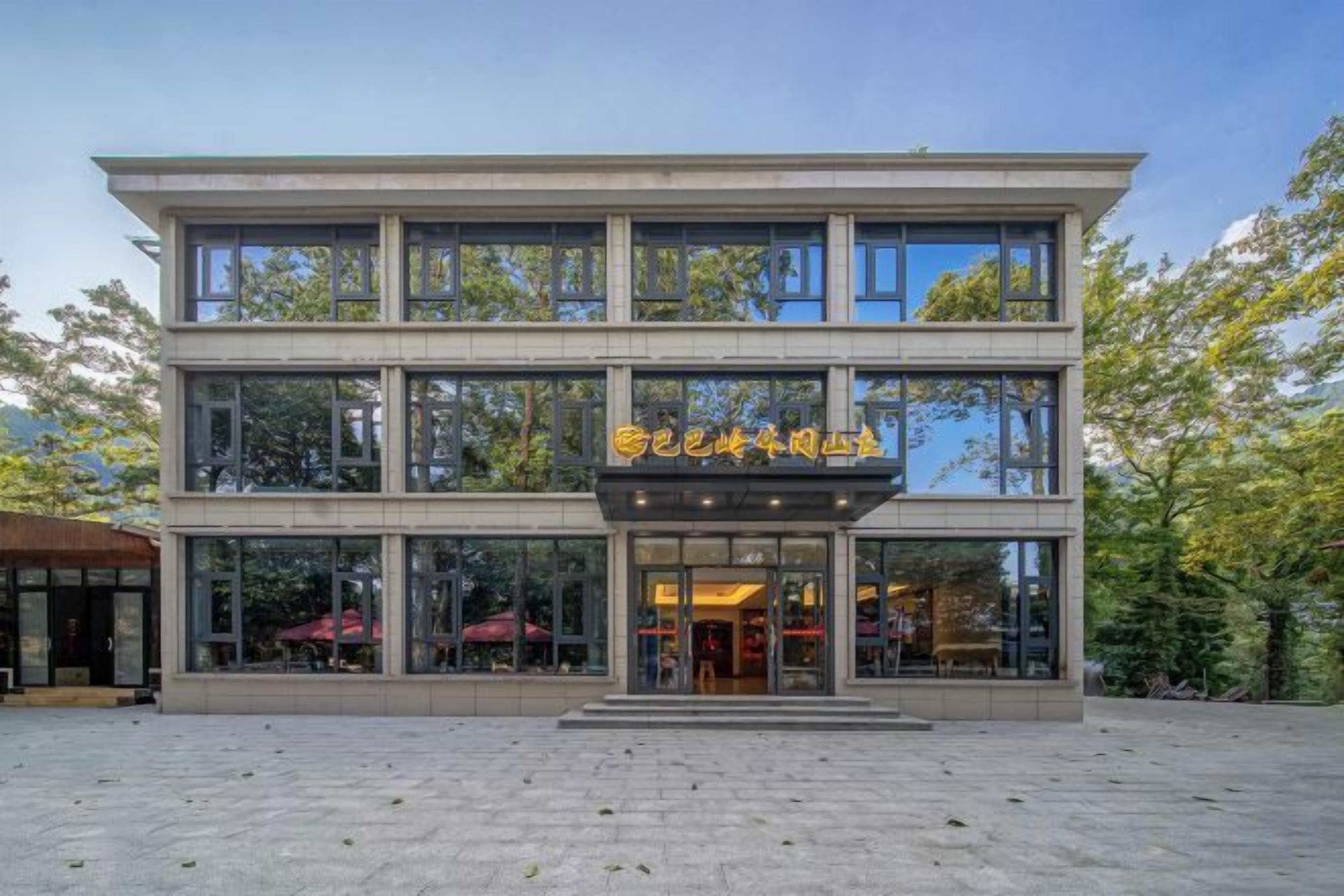 A modern building with a glass facade, a prominent entrance, and outdoor seating visible through the windows.