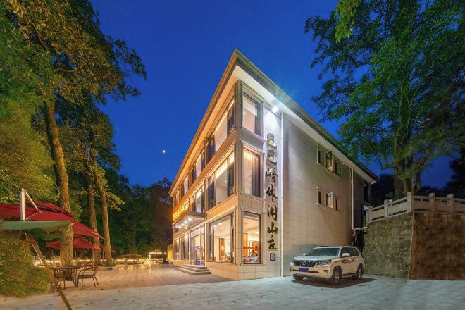 A modern hotel with a well-lit entrance, outdoor seating, and a stone wall.