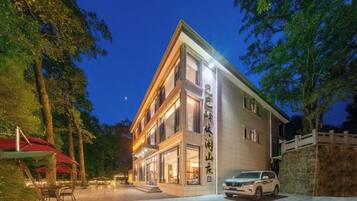 A modern hotel with a well-lit entrance, outdoor seating, and a stone wall.