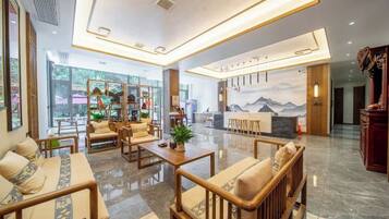 A modern hotel lobby with seating areas, a reception desk, and a mural on the wall.