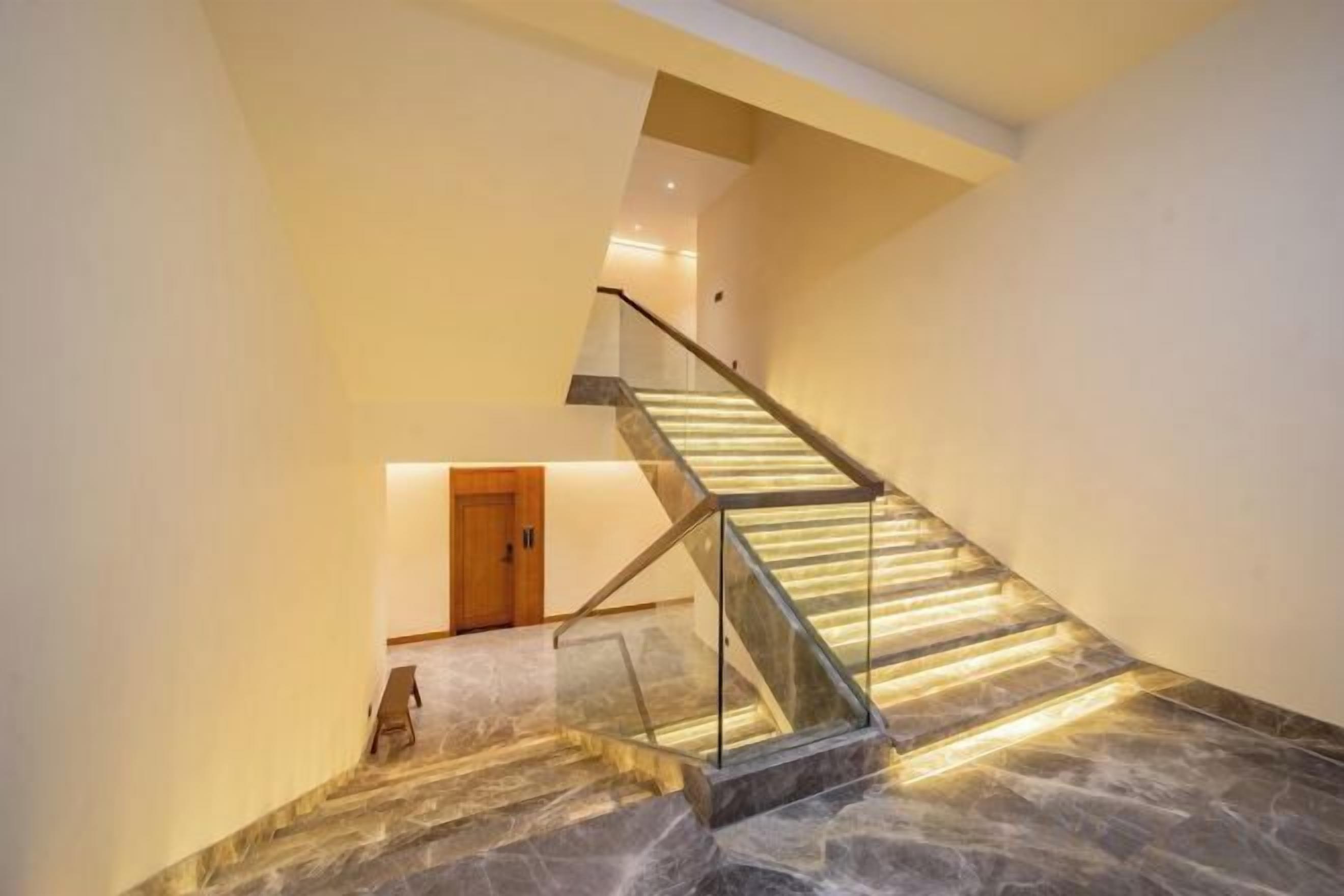 Una escalera con barandillas de vidrio y peldaños de mármol, que conduce a un rellano con una puerta.