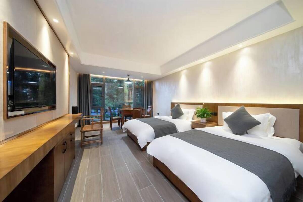 A modern hotel room with two beds, a TV, a desk, and a view of the outdoors.