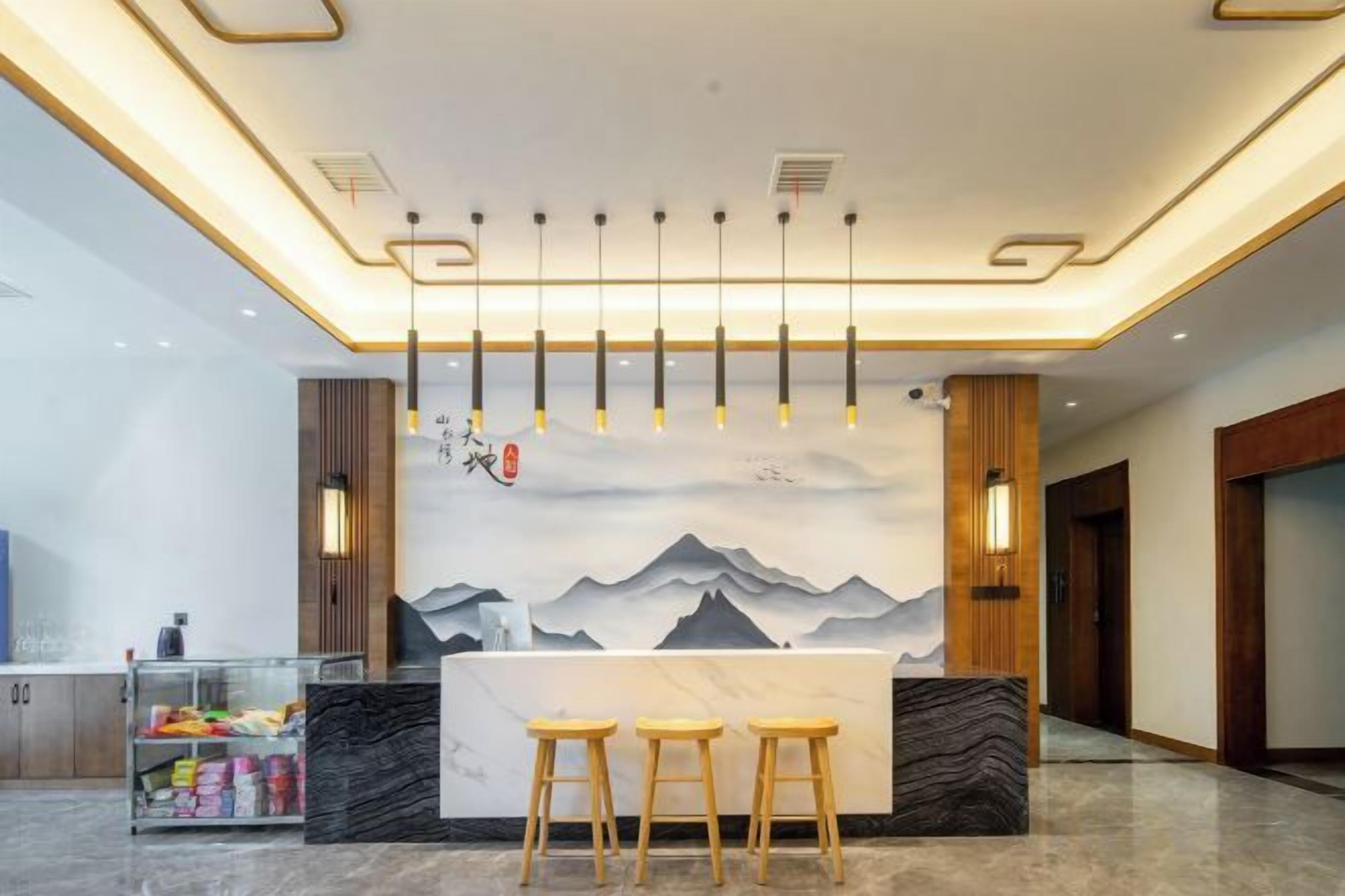 A reception area with a counter, bar stools, a wall with a mountain painting, and hanging pendant lights.