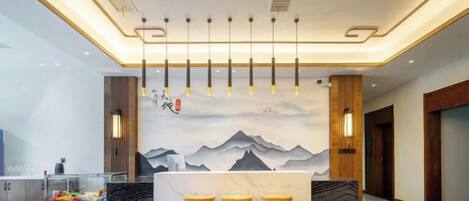 A reception area with a counter, bar stools, a wall with a mountain painting, and hanging pendant lights.