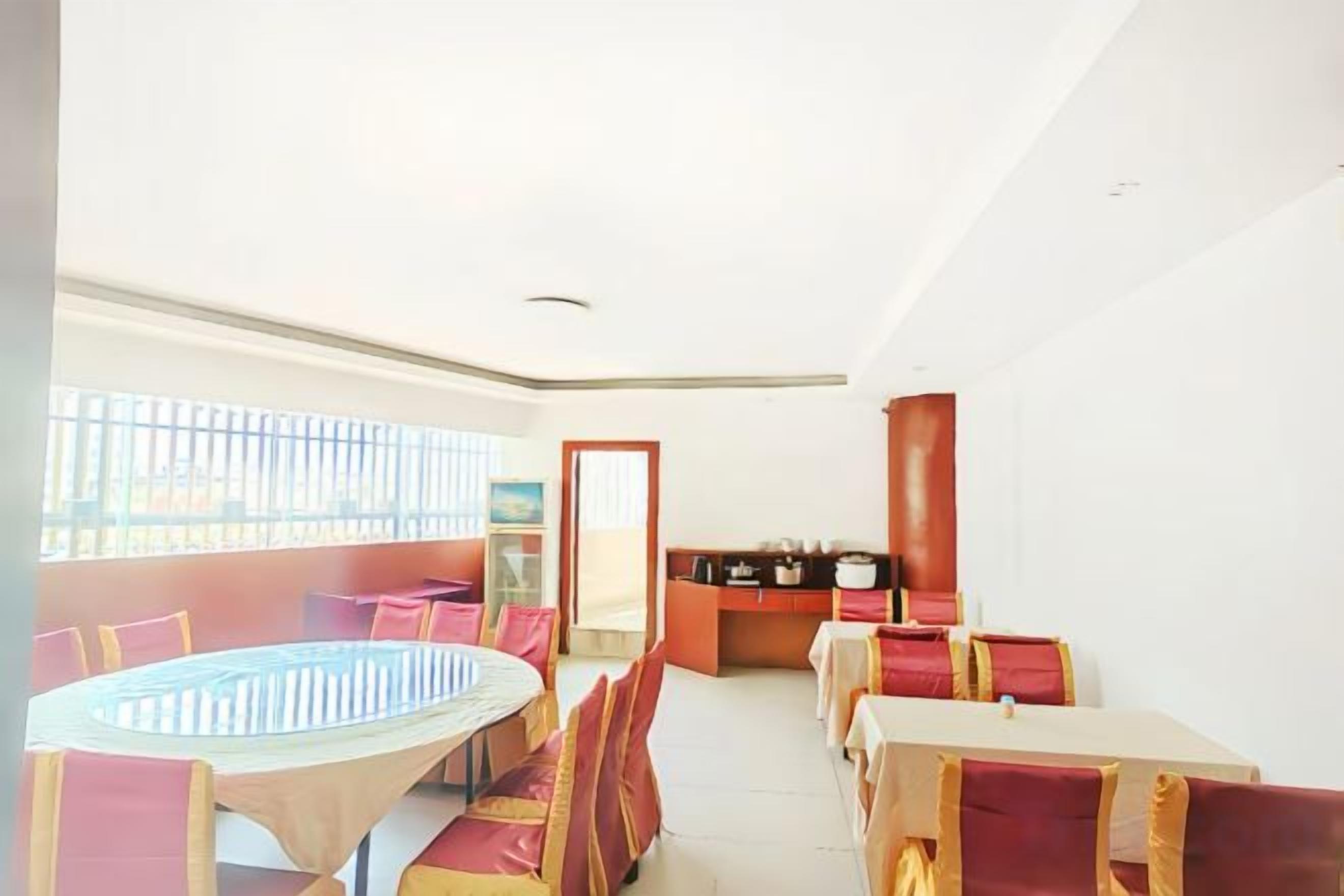 A dining area with a round table and chairs, a kitchen in the background, and a view through a window.